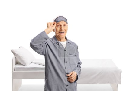 Téléchargez les photos : Homme âgé en pyjama enlevant un masque de sommeil isolé sur fond blanc - en image libre de droit