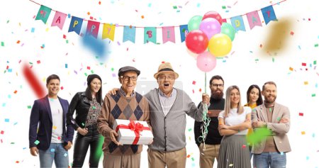Foto de Amigos mayores con un regalo y globos celebrando cumpleaños con un grupo de jóvenes aislados sobre fondo blanco - Imagen libre de derechos