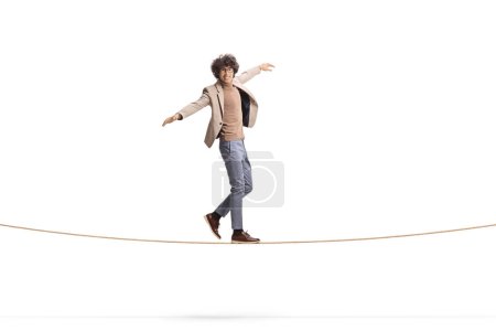Full length portrait of a young man with curly hair walking on a tightrope and smiling isolated on white background