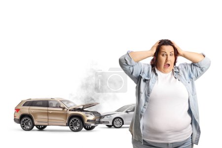 Téléchargez les photos : Femme corpulente choquée tenant sa tête près d'un accident de voiture isolé sur fond blanc - en image libre de droit