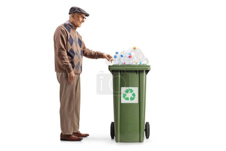 Foto de Foto de perfil completo de un hombre mayor lanzando una botella de plástico en una papelera de reciclaje aislada sobre fondo blanco - Imagen libre de derechos