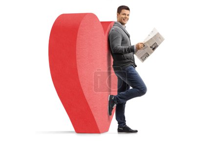 Foto de Retrato completo de un tipo con un periódico apoyado sobre un corazón rojo aislado sobre fondo blanco - Imagen libre de derechos