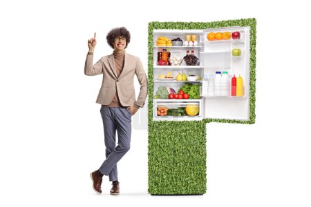 Photo for Young man getsuring pointing up nexto to a green eco-friendly fridge isolated on white background - Royalty Free Image