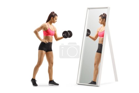 Foto de Ajuste joven hembra ejercitando el entrenamiento con pesas con una mancuerna delante de un espejo aislado sobre fondo blanco - Imagen libre de derechos