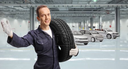 Téléchargez les photos : Mécanicien automobile tenant un pneu de voiture dans un garage - en image libre de droit