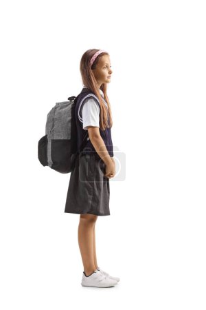Ganztägige Profilaufnahme eines Schulmädchens in Uniform mit einem Rucksack auf den Schultern, isoliert auf weißem Hintergrund