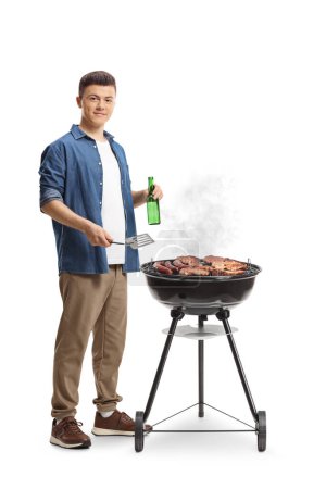 Téléchargez les photos : Jeune homme faisant un barbecue et tenant une bouteille de bière isolée sur fond blanc - en image libre de droit