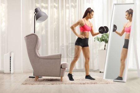 Téléchargez les photos : S'adapter jeune entraînement de poids d'exercice féminin avec un haltère devant un miroir à la maison - en image libre de droit