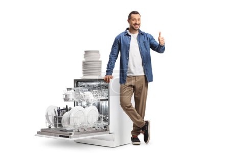 Photo for Guy showing thumbs up next to a dishwasher isolated on white background - Royalty Free Image