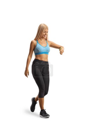 Foto de Mujer joven delgada caminando y comprobando su pulsera de fitness aislada sobre fondo blanco - Imagen libre de derechos