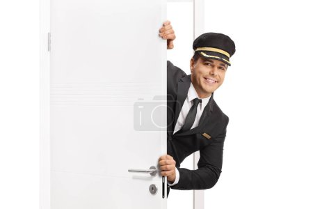 Téléchargez les photos : Bellboy debout derrière une porte blanche isolée sur fond blanc - en image libre de droit