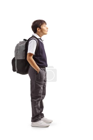 Ganztägige Profilaufnahme eines Schülers in Uniform, der mit den Händen in den Taschen steht und isoliert auf weißem Hintergrund nach oben schaut