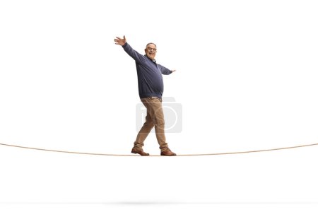 Foto de Tiro de longitud completa de un hombre maduro caminando sobre una cuerda aislada sobre fondo blanco, mantener el concepto de equilibrio - Imagen libre de derechos