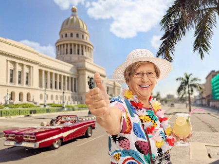 Alegre turista maduro sosteniendo un cóctel y haciendo un gesto de pulgar hacia arriba en La Habana, Cuba