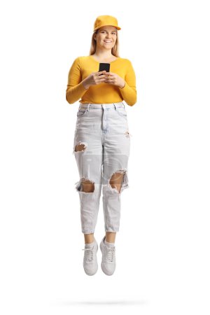 Téléchargez les photos : Heureuse femelle tenant un smartphone et sautant haut isolé sur fond blanc - en image libre de droit