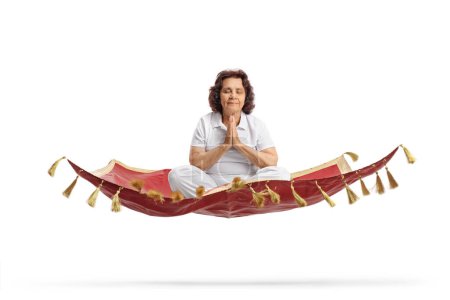 Téléchargez les photos : Femme âgée méditant sur un tapis magique flottant isolé sur fond blanc - en image libre de droit