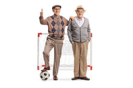 Téléchargez les photos : Hommes âgés debout avec un ballon de football devant un but et les pouces geste vers le haut isolé sur fond blanc - en image libre de droit