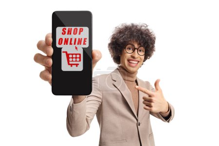 Téléchargez les photos : Heureux jeune homme aux cheveux bouclés pointant vers un smartphone avec application de shopping en ligne isolé sur fond blanc - en image libre de droit