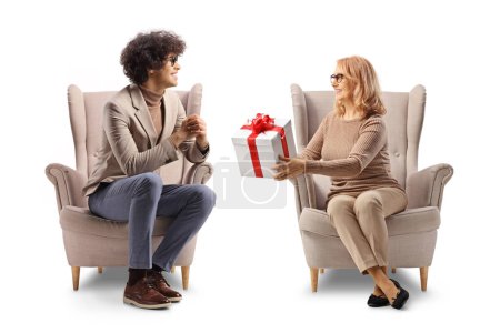 Téléchargez les photos : Femme assise dans un fauteuil et donnant un cadeau à un jeune homme isolé sur fond blanc - en image libre de droit