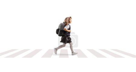 Téléchargez les photos : Plan de profil complet d'une écolière en uniforme portant un sac à dos et courant à un passage à niveau isolé sur fond blanc - en image libre de droit