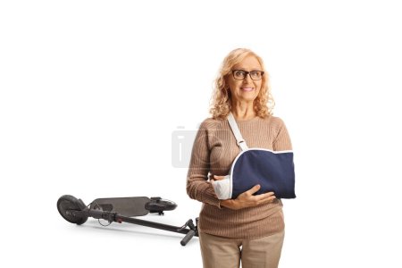 Photo for Mature woman with a broken arm in a sling injured from electric scooter fall isolated on white background - Royalty Free Image