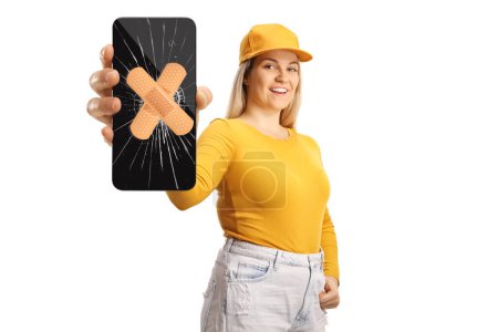 Téléchargez les photos : Adolescente tenant un smartphone avec verre d'écran cassé et bandage isolé sur fond blanc - en image libre de droit