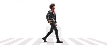 Téléchargez les photos : Profil complet d'un jeune homme en veste de cuir marchant sur un piéton et portant un casque de moto isolé sur fond blanc - en image libre de droit