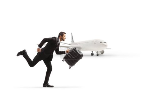 Téléchargez les photos : Homme d'affaires courant et portant une valise près d'un avion isolé sur fond blanc - en image libre de droit