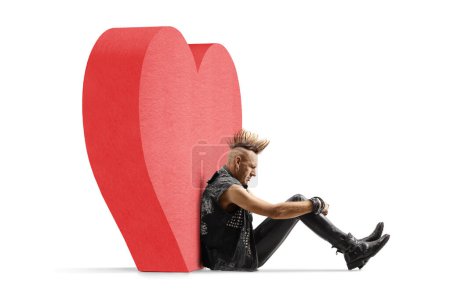 Téléchargez les photos : Punk rocker avec un mohawk assis sur le sol et appuyé sur un cœur rouge isolé sur fond blanc - en image libre de droit
