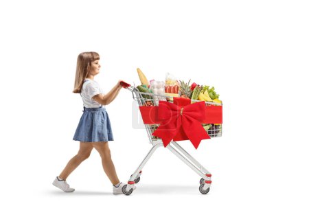 Téléchargez les photos : Petite fille poussant un panier avec des produits alimentaires isolés sur fond blanc - en image libre de droit