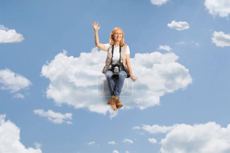 Foto de Mujer foto periodista sentada en una nube y saludando - Imagen libre de derechos