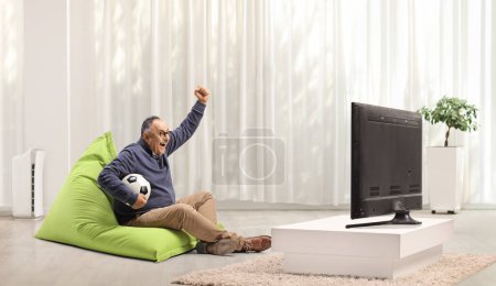 Photo for Mature man at home cheering and watching football on tv - Royalty Free Image