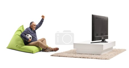Foto de Hombre maduro sentado en un sillón bolso de frijol animando y viendo fútbol en la televisión - Imagen libre de derechos