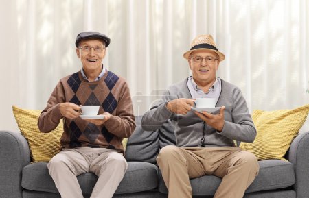 Photo for Elderly men sitting on a sofa at home and having a cup of tea - Royalty Free Image