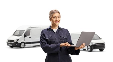 Téléchargez les photos : Travailleuse mécanicienne portant l'uniforme général et tenant un ordinateur portable devant des fourgonnettes isolées sur fond blanc - en image libre de droit