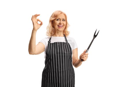 Téléchargez les photos : Femme portant un tablier tenant une fourchette et geste ok signe isolé sur fond blanc - en image libre de droit