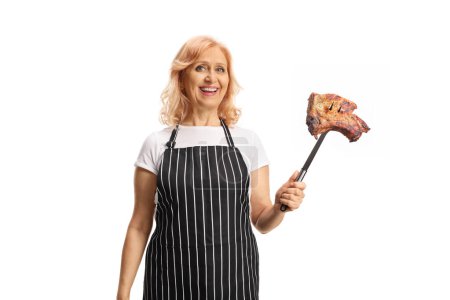 Foto de Mujer usando un delantal y sosteniendo un filete de cerdo a la parrilla con un tenedor aislado sobre fondo blanco - Imagen libre de derechos
