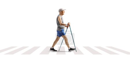 Téléchargez les photos : Photo de profil pleine longueur d'un homme mature traversant une rue avec des bâtons de trekking isolés sur fond blanc - en image libre de droit