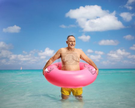Photo for Smiling mature man in the sea wearing swimming shorts and inflatable flamingo rubber ring - Royalty Free Image