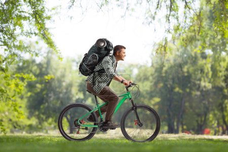 Photo for Full length profile shot of a guy with a backpack riding a bicycle in a park - Royalty Free Image