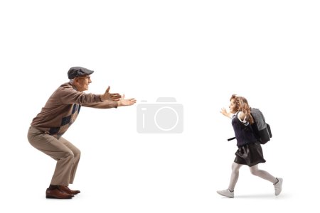 Photo for Full length profile shot of a schoolgirl with a backpack running towards her grandfather isolated on white backgroun - Royalty Free Image