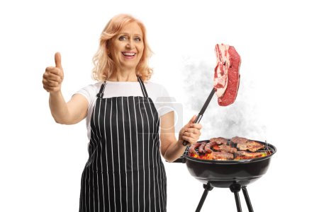 Foto de Mujer asando carne en una barbacoa y sosteniendo un filete crudo con un tenedor aislado sobre fondo blanco - Imagen libre de derechos