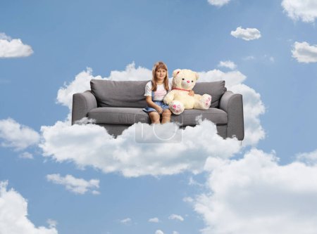Foto de Chica con un gran osito de peluche sentado en un sofá en las nubes - Imagen libre de derechos