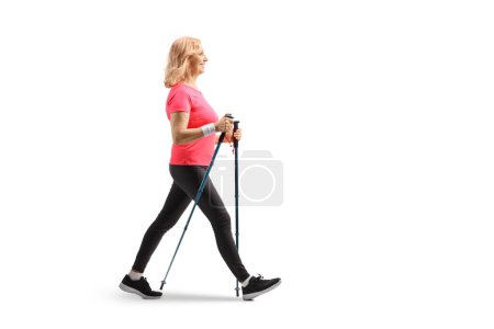 Photo for Full length profile shot of a middle aged woman walking with trekking poles isolated on white background - Royalty Free Image