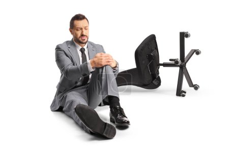Téléchargez les photos : Chaise de bureau sur le sol et un homme d'affaires tenant son genou douloureux isolé sur fond blanc - en image libre de droit