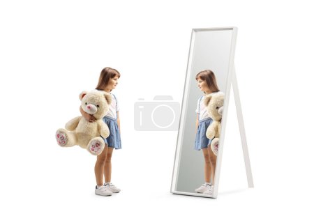 Foto de Chica sosteniendo un gran osito de peluche y mirando un espejo aislado sobre fondo blanco - Imagen libre de derechos