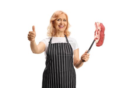 Photo for Woman holding a raw meat steak on a fork and gesturing thumbs up isolated on white background - Royalty Free Image