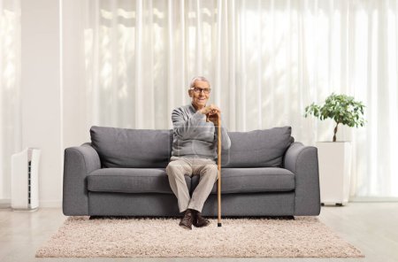 Foto de Hombre mayor sentado en un sofá en casa y sonriendo - Imagen libre de derechos