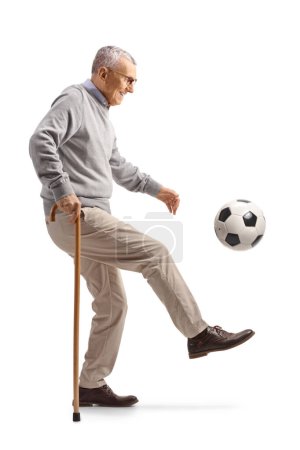 Téléchargez les photos : Homme âgé appuyé sur une canne à pied et le coup de pied d'un football isolé sur fond blanc - en image libre de droit