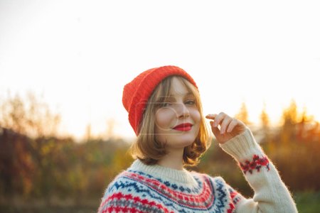 Téléchargez les photos : Portrait hivernal lumineux d'une belle jeune femme en bonnet rouge tricoté sur fond d'arbres de Noël. Eco Noël, vacances d'hiver. - en image libre de droit